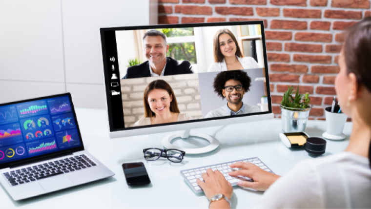 Woman in white top attending a video conference from home with 2 screens