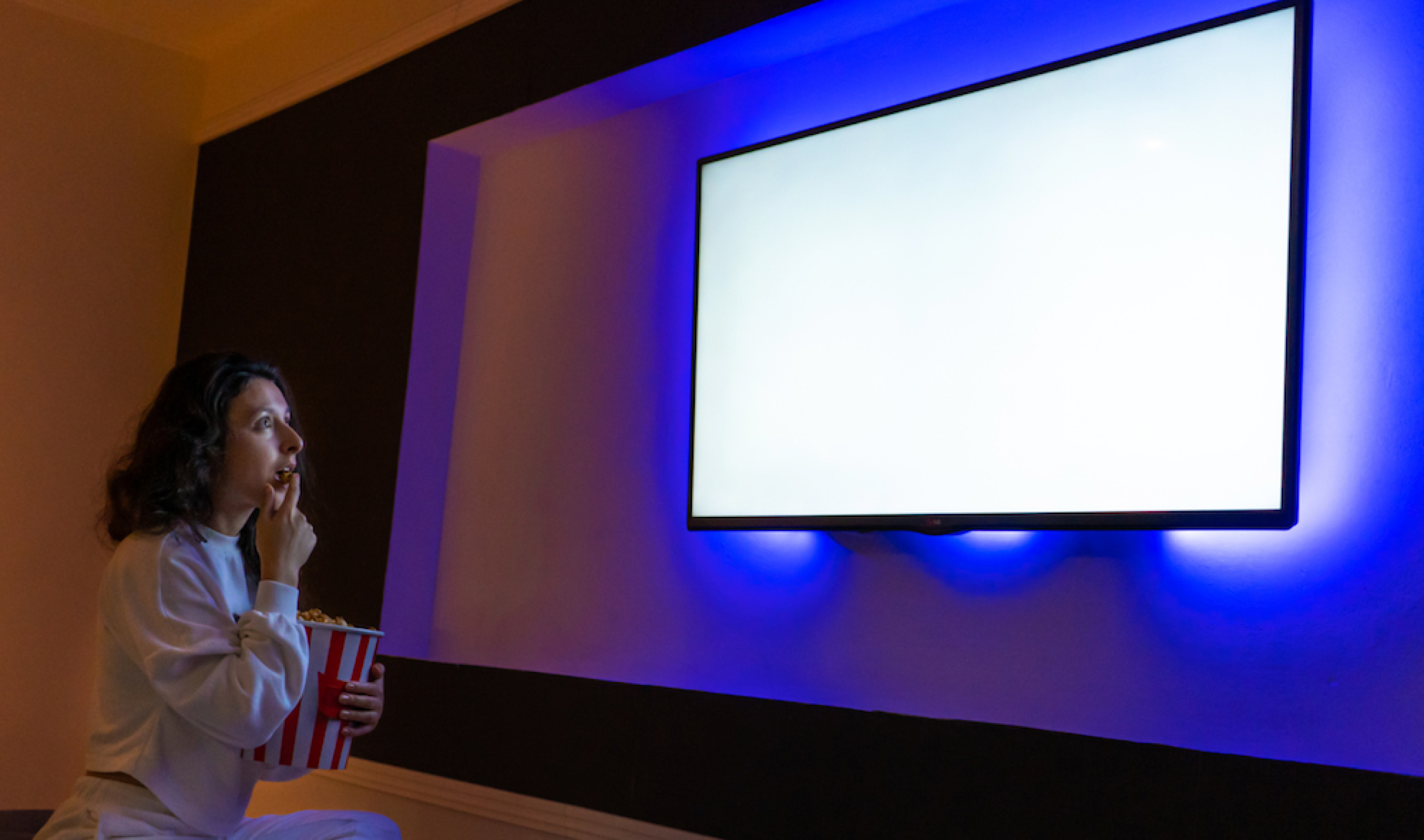 Woman with bag of popcorn looking at a blank home cinema screen with puzzled expression on her face